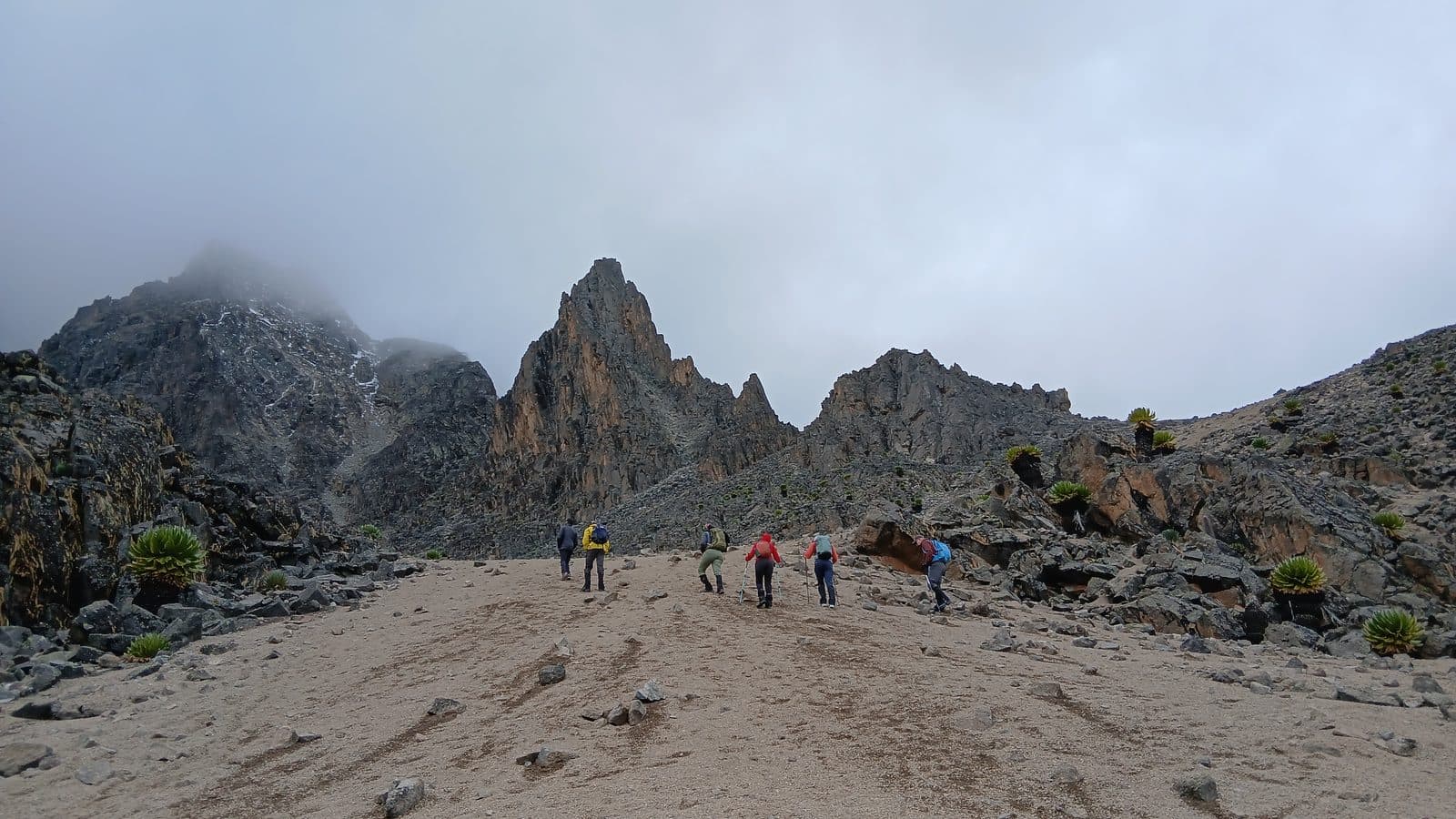 Trekkers crossing a rocky valley below mist-covered Mount Kenya peaks