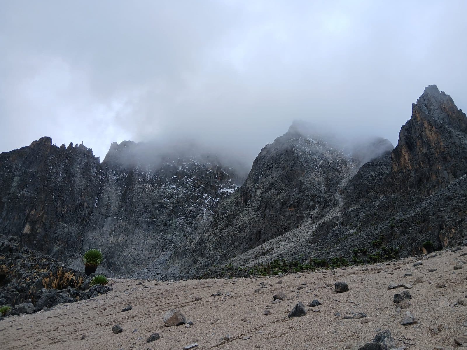 Jagged Mount Kenya peaks disappearing into cloud above a gravel valley