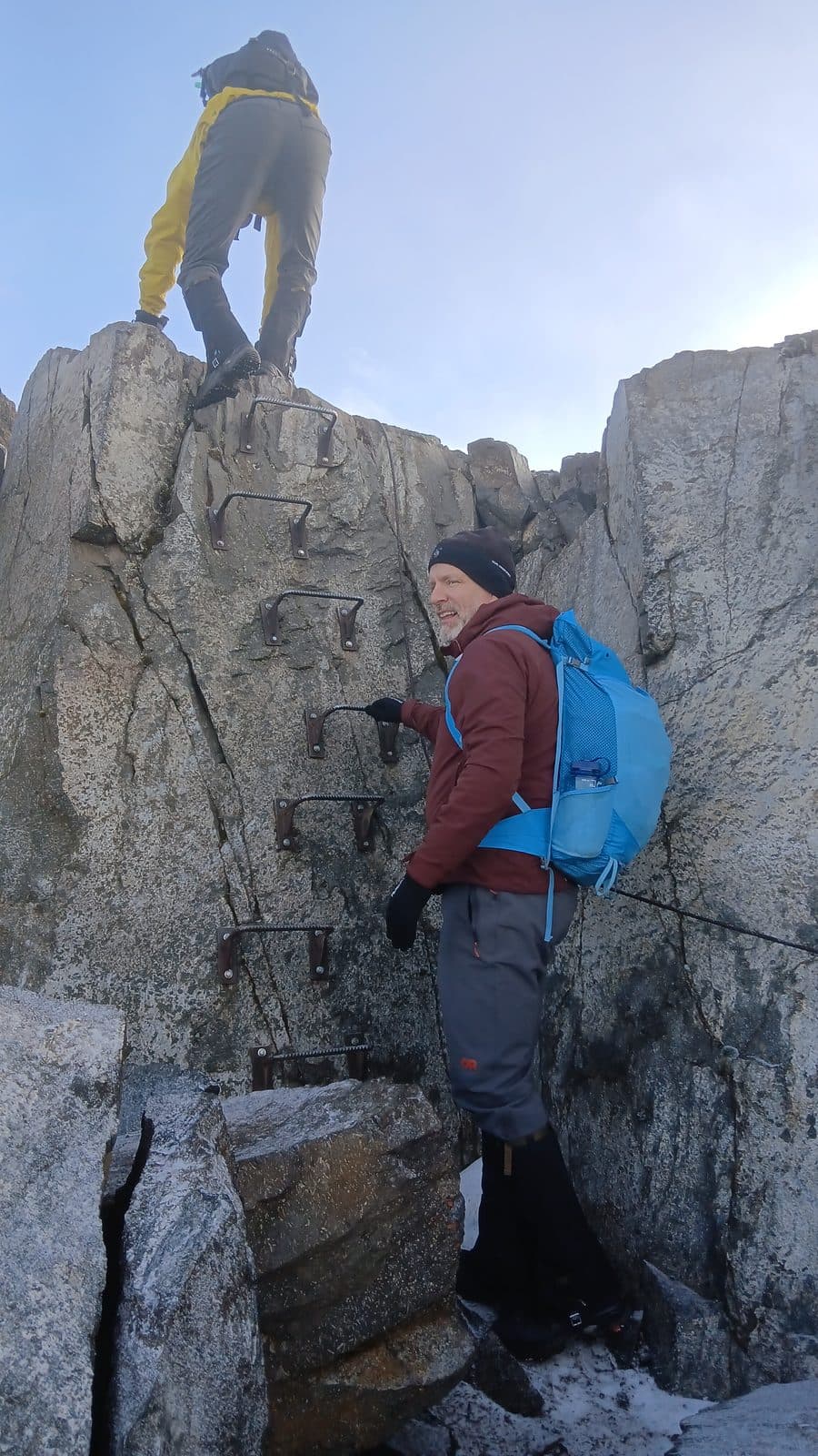 Trekker scrambling up a rock face while a guide waits below
