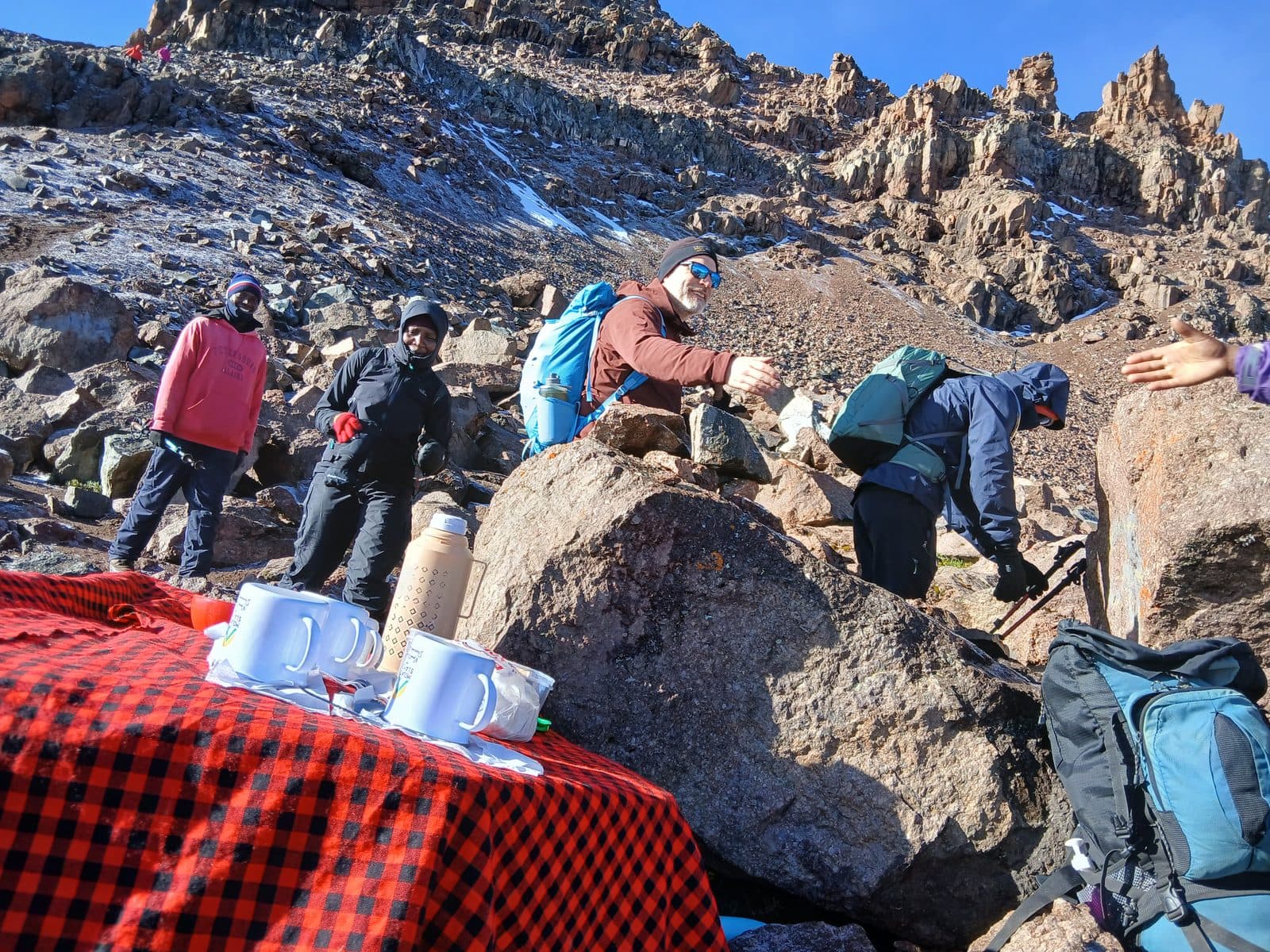 Trekkers resting among boulders beside a tea break on a red Maasai shuka