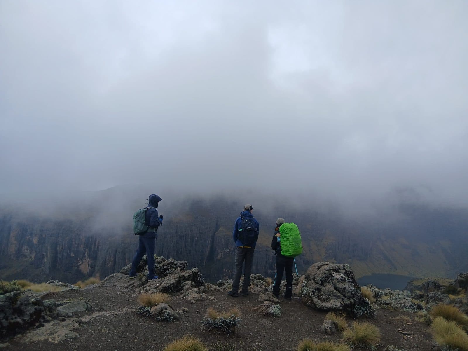 Three trekkers standing on a rocky viewpoint above a cloud-filled valley