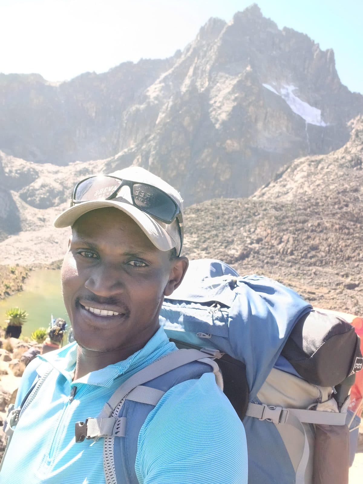 Selfie of a smiling guide with a large pack below Mount Kenya's snowy peaks