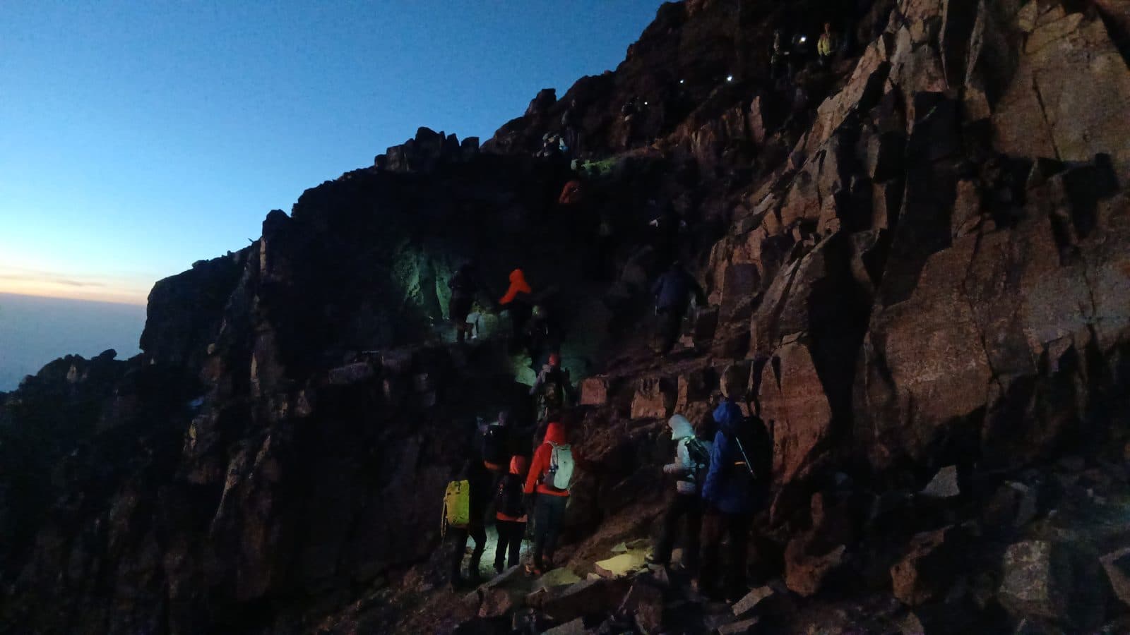 Trekkers with headlamps climbing a dark rock face before dawn