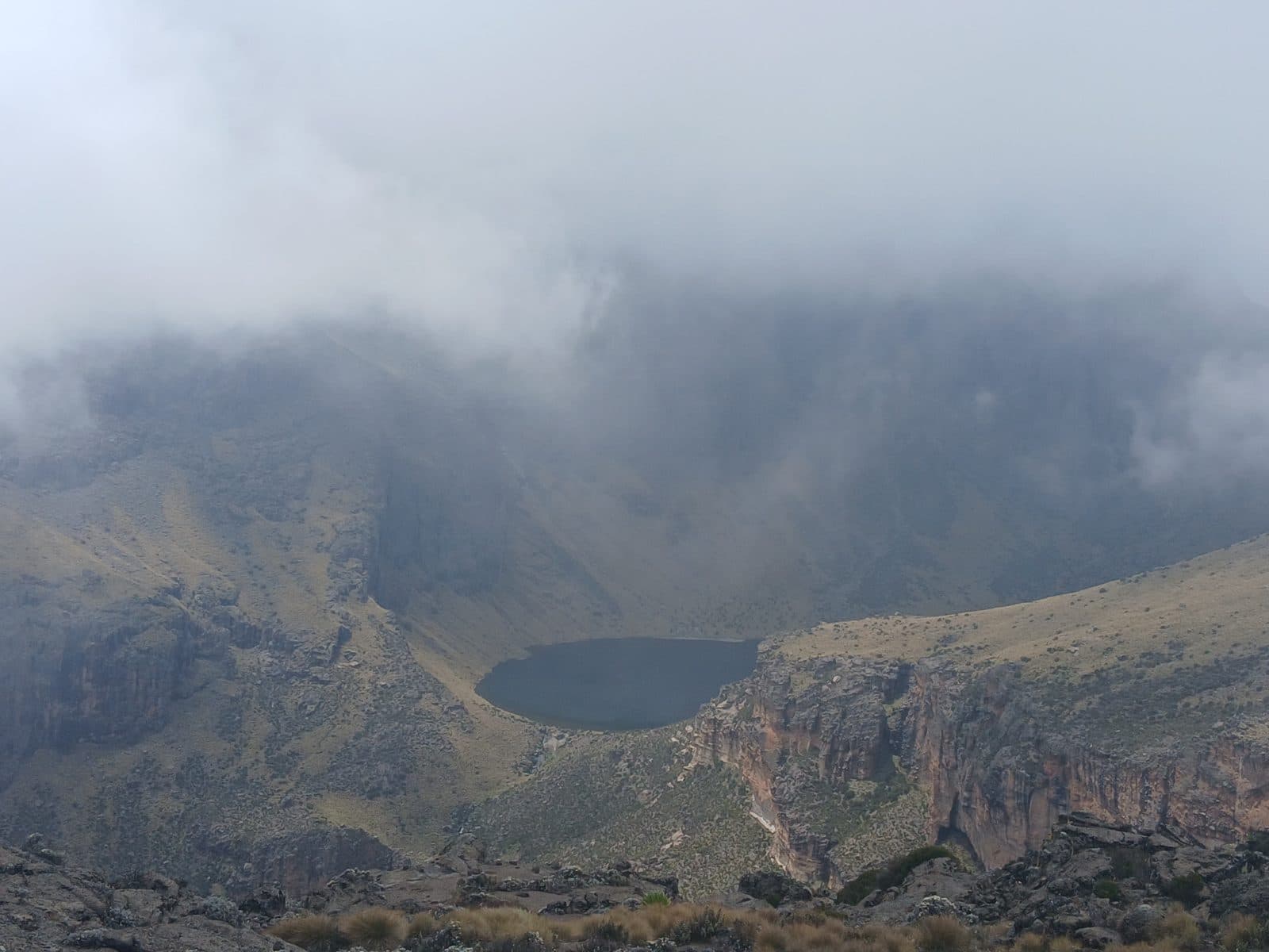 Small lake far below in a cloud-filled mountain valley