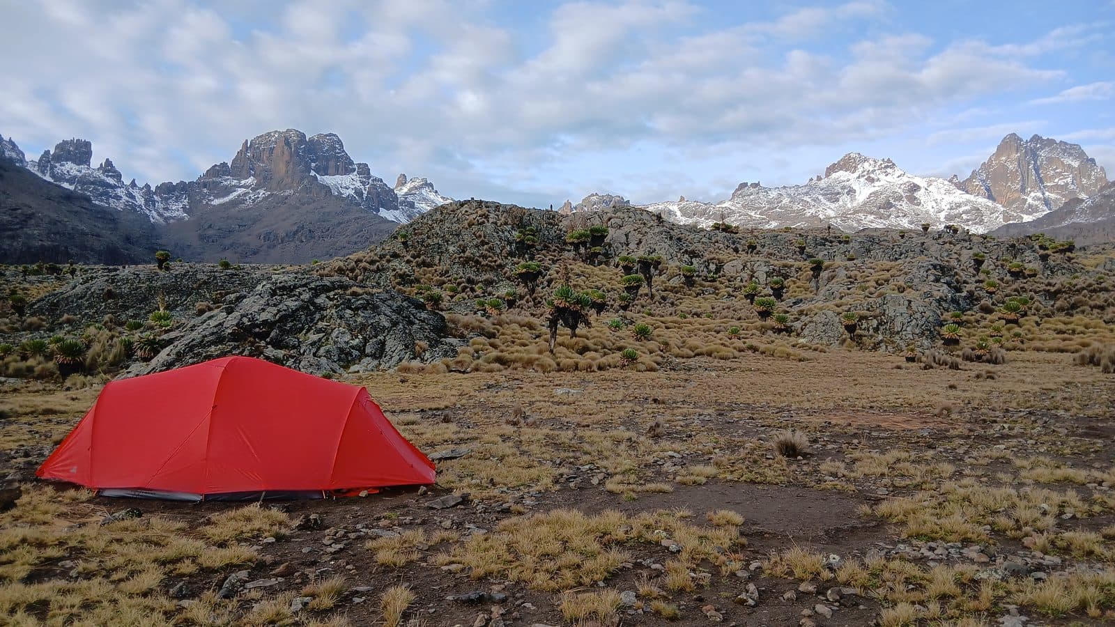 Red tent on the moorland with snowy Mount Kenya peaks on the horizon