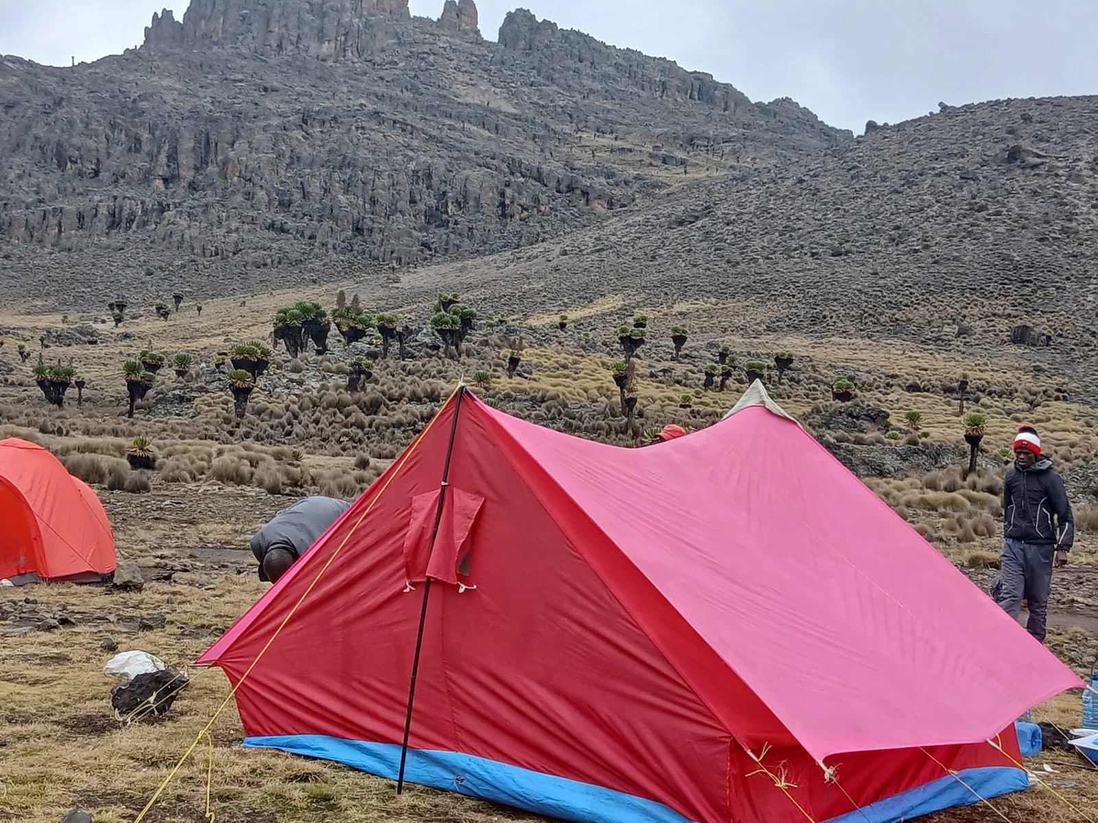Large red tent and a trekker at a rocky high camp