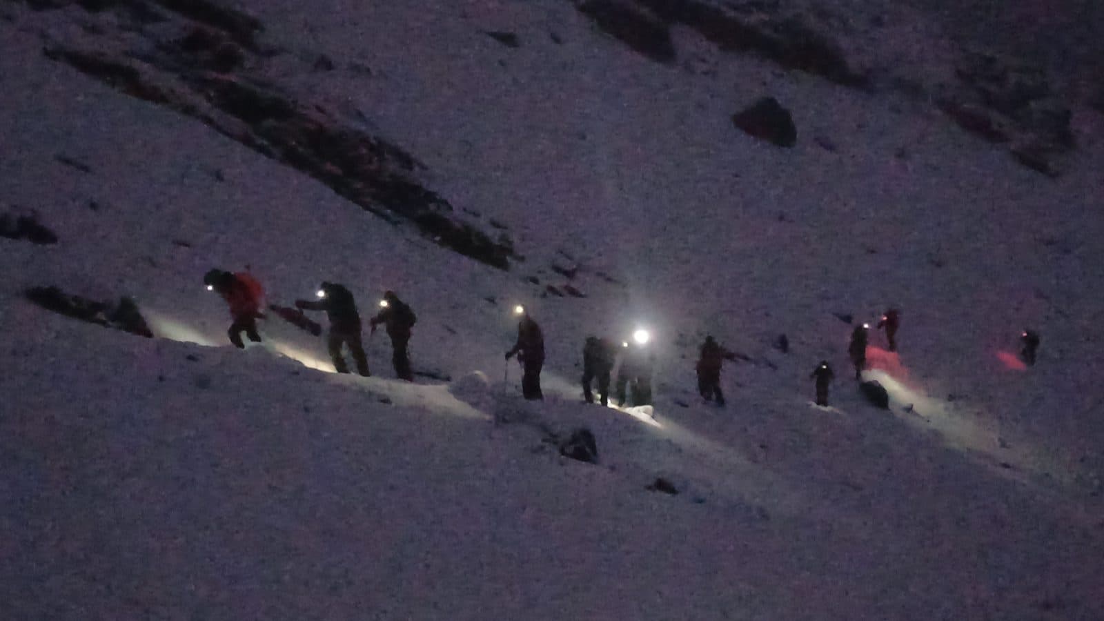 Line of headlamps climbing a snowy slope before sunrise