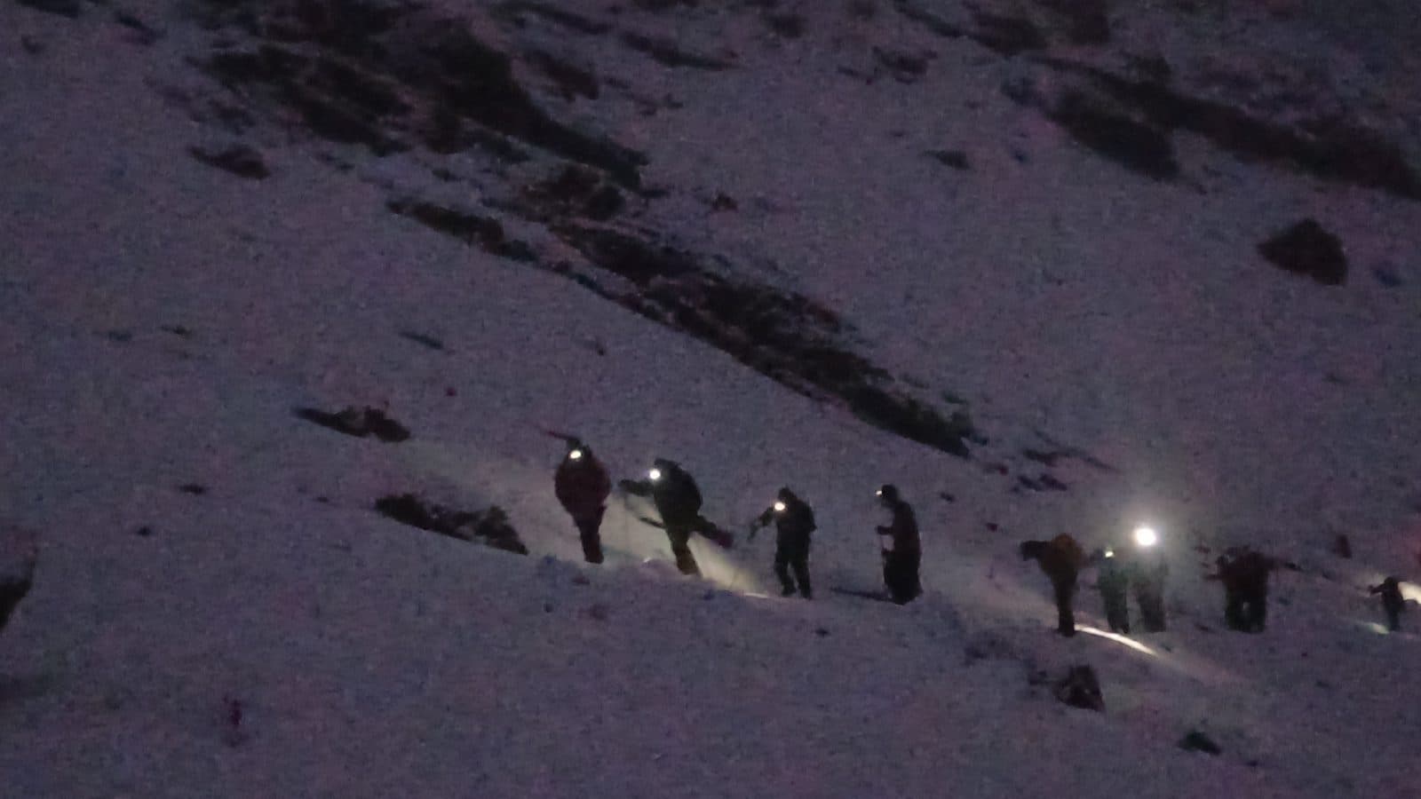 Trekkers with headlamps ascending a snow-covered slope in the dark