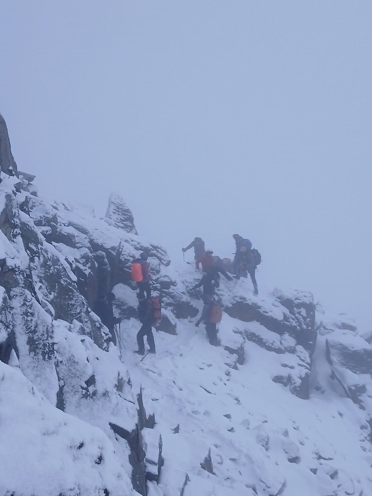Trekkers scrambling up snow-covered rocks in cloud