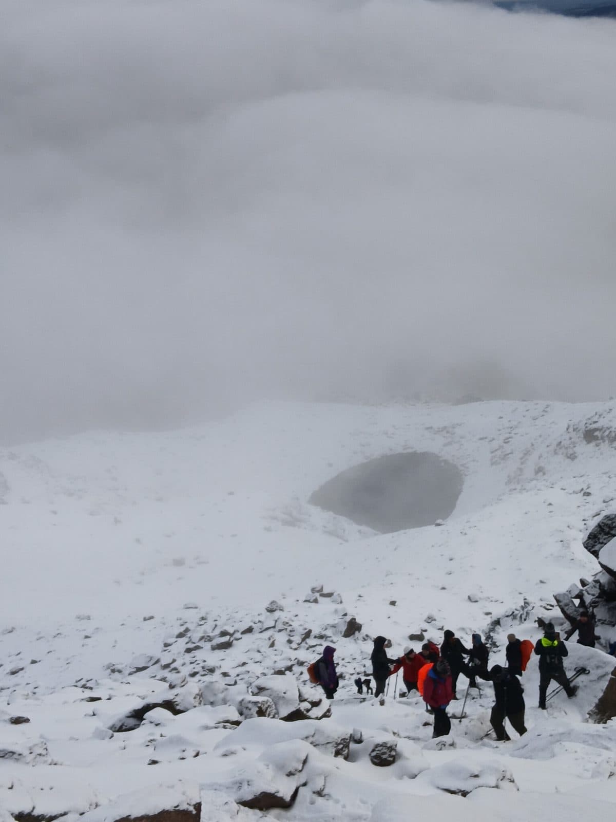Group of trekkers crossing snow in a cloud-filled crater