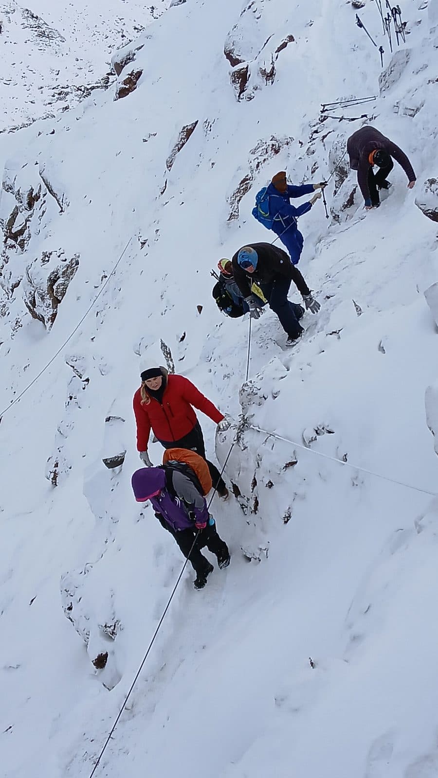 Trekkers holding a fixed cable on a steep snowy slope