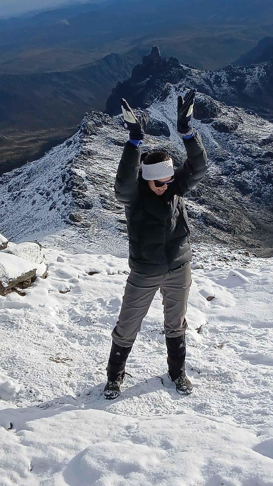 Trekker celebrating with arms raised on a snowy summit