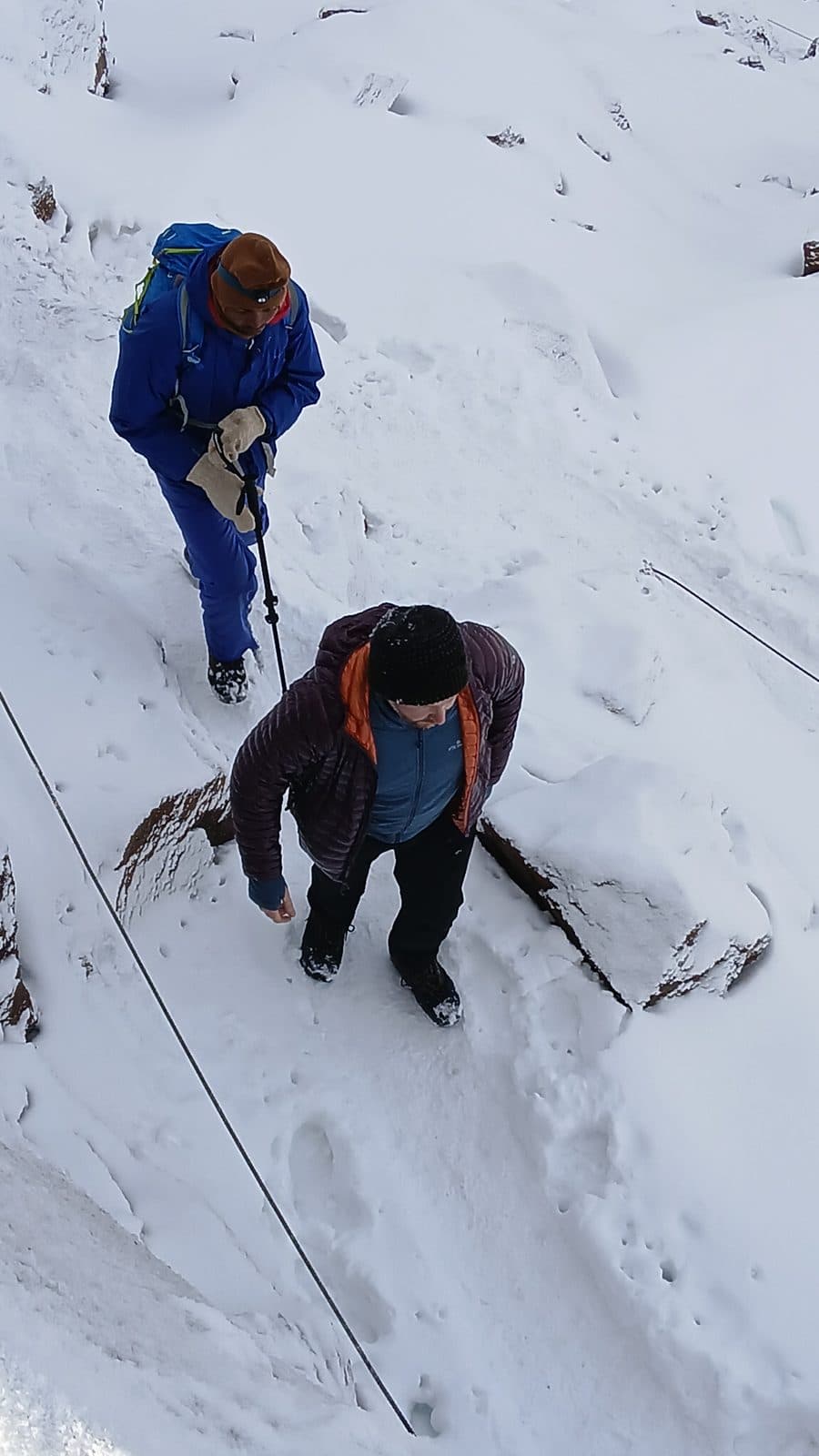 Two trekkers descending a snowy slope with a fixed cable