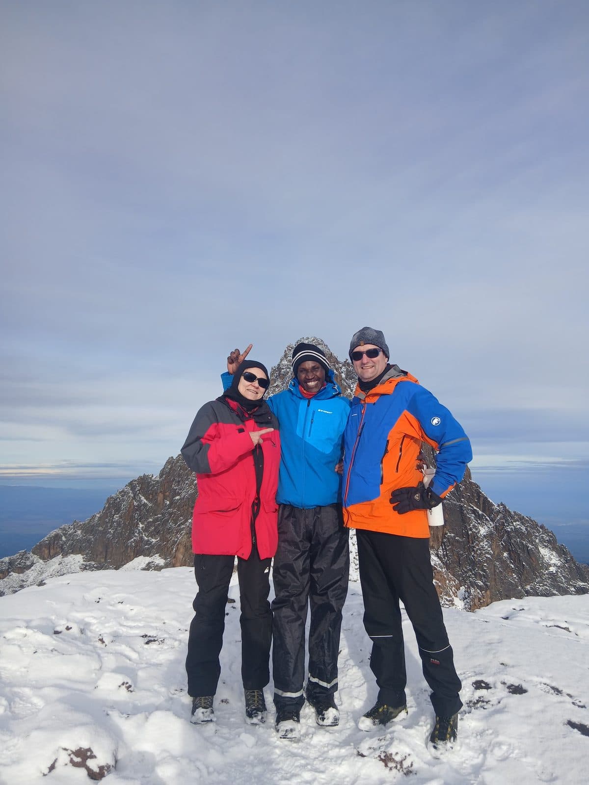 Three trekkers on a snowy summit with the plains far below