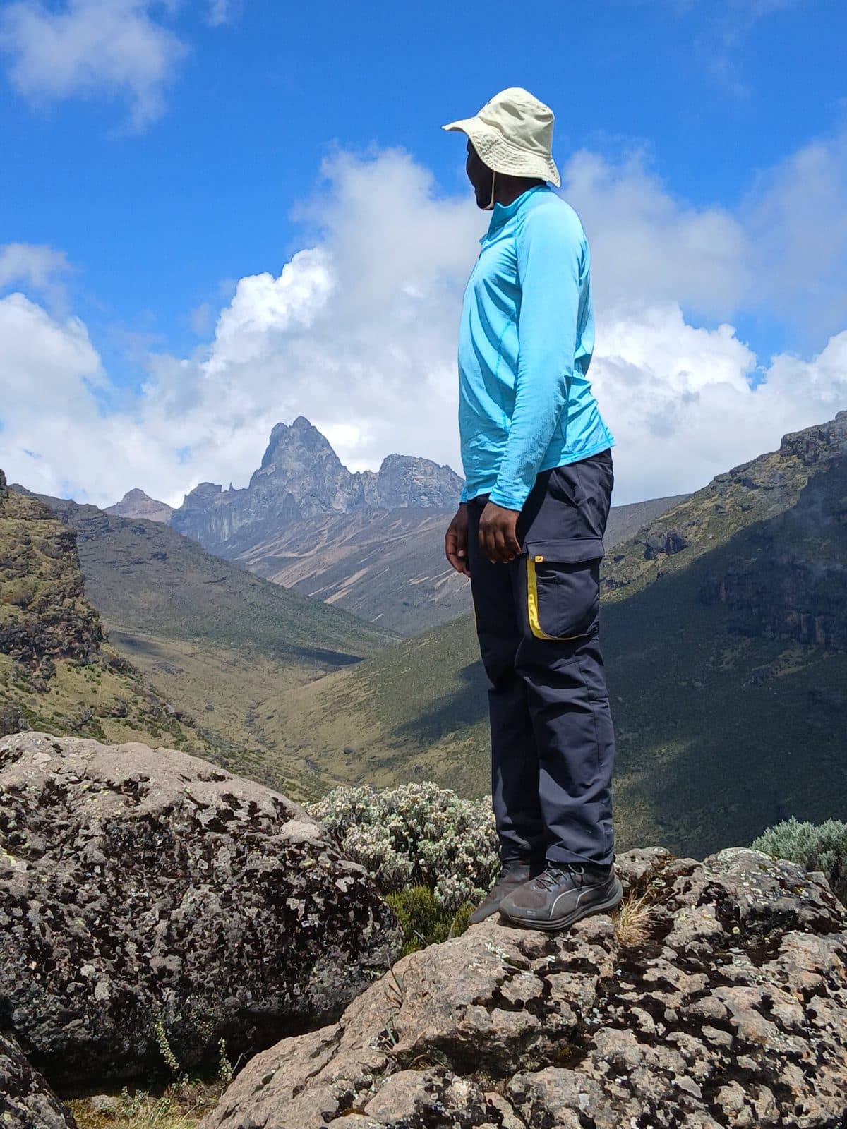 Guide in a sun hat looking out over a valley toward Mount Kenya