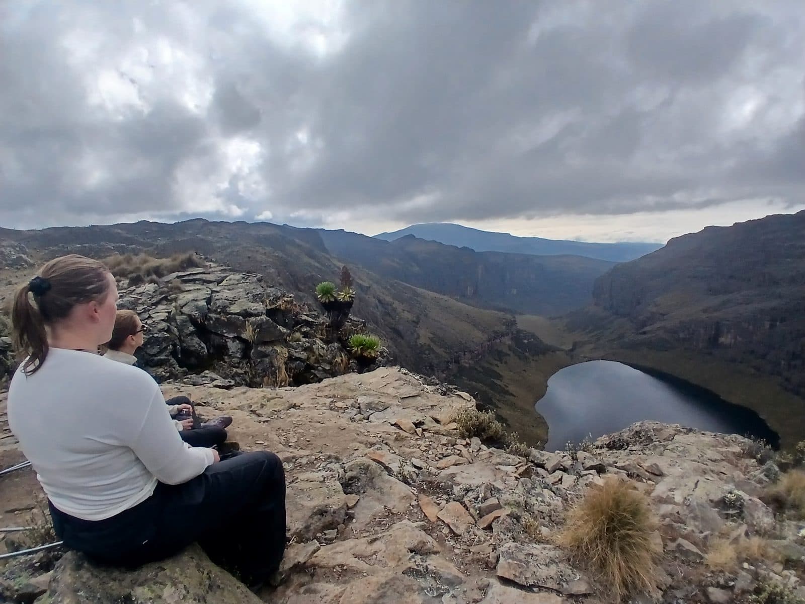 Trekker sitting on rocks above a lake in a deep mountain valley