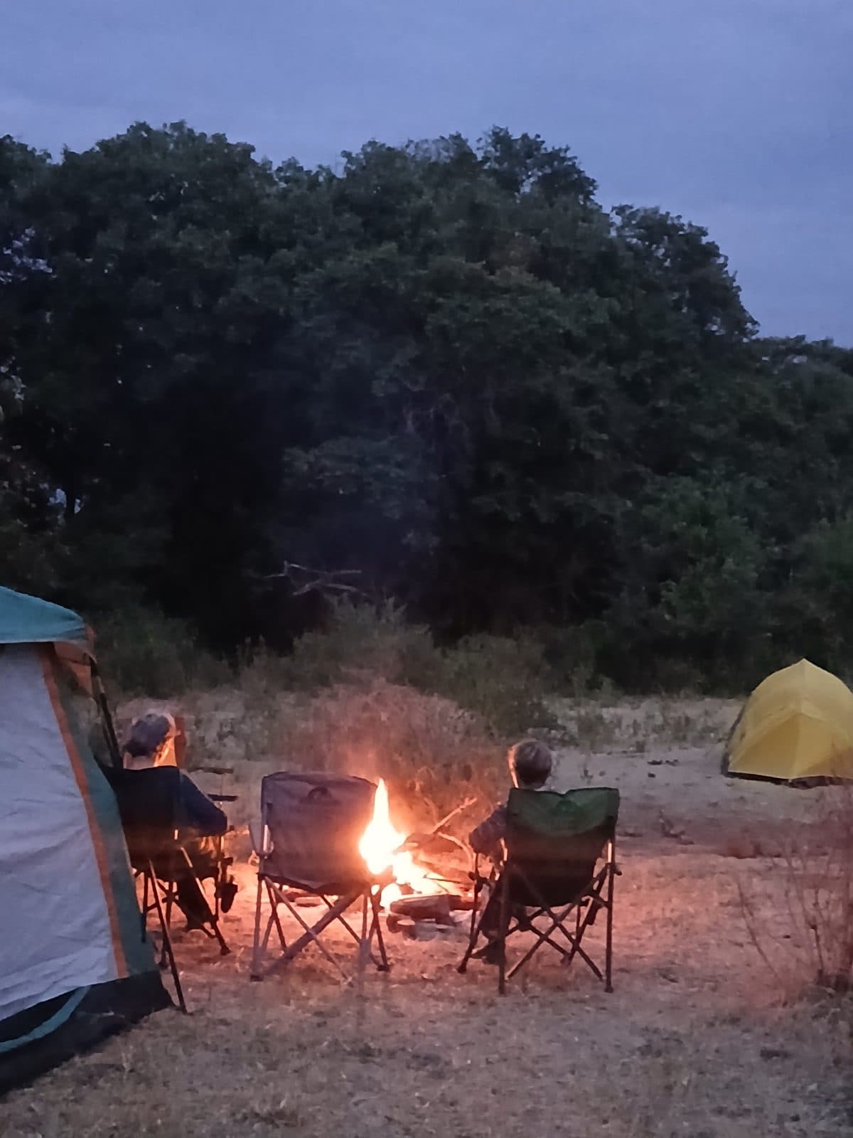 Trekkers relaxing around a campfire beside their tents at dusk