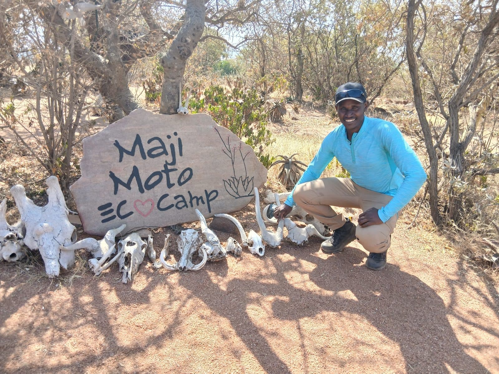 Guide crouching by the Maji Moto Eco Camp sign and animal skulls